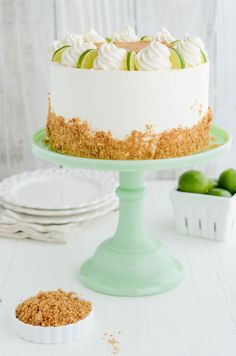 a white cake with limes and whipped cream on top sitting on a green pedestal