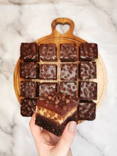 a person holding up a piece of chocolate brownie on top of a wooden cutting board