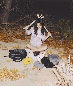 a woman sitting on the ground with her arms crossed and holding two baseball bats in one hand