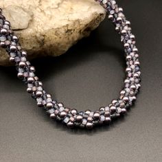 "This necklace is a mute blend of dusty mauve, grey & taupe seed beads, which accent the gorgeous center segment of 4mm round silky mauve Swarovski crystal pearls. The necklace measures 17 1/2\" long, and includes a 2 1/2\" extender, for a maximum length of 19\". Bali style sterling silver end caps give the finishing touch to this beautiful piece. The necklace is created using an ancient Japanese braiding technique called Kumihimo. A wooden stand called a marudai is used as a loom. Multiple cords are beaded with carefully selected color combinations of beads and then wound around wooden bobbins. The bobbins are weighted and counterweighted so they spread evenly across the marudai. The weaving is done by lifting the cords across the marudai in pairs in a selected pattern based on the desire Adjustable Beaded Purple Pearl Necklace, Adjustable Purple Beaded Pearl Necklace, Japanese Braiding, Office Jewelry, Portrait Necklace, Necklace Cat, Braided Necklace, Taupe Grey, Cat Pendant