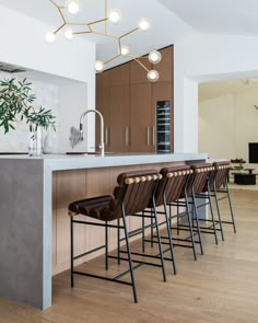 a modern kitchen with bar stools and an island in the middle is lit by pendant lights