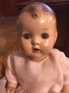 an old porcelain baby doll sitting on the ground in front of a wooden table and cabinet