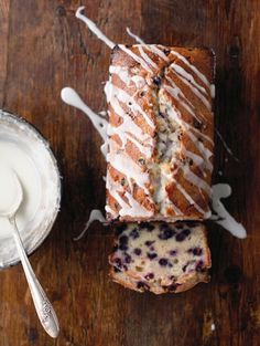 a loaf of blueberry bread next to a bowl of yogurt on a wooden table