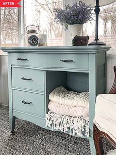 a blue dresser with two drawers and a clock on it's top, in front of a window