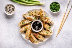 a white plate topped with dumplings covered in sauce and garnished with green onions