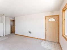 an empty living room with white walls and wood trim on the door, carpeted floor