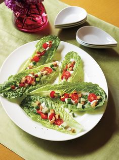 lettuce wraps with tomatoes and other vegetables on a white plate next to plates