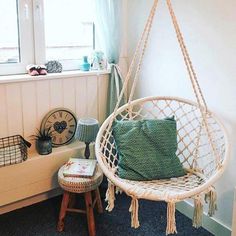 a white hanging chair next to a window in a room with blue carpet and green pillows