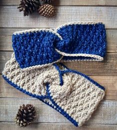 two crocheted mittens are sitting on a wooden surface next to pine cones