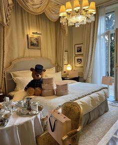 a teddy bear sitting on top of a bed next to a table filled with tea