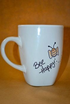 a white coffee cup with the words be happy written on it and a honeybee