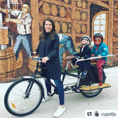 three people on a bike in front of a mural