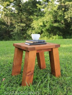 a small wooden table sitting in the grass with two books on it and a coffee cup on top