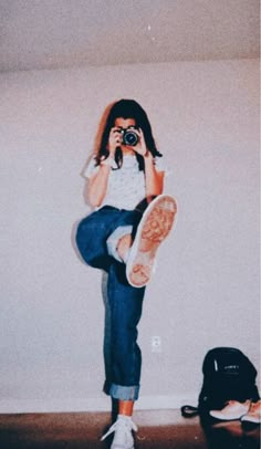 a woman taking a photo with her camera in front of a wall and a backpack