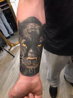 a person with a tattoo on their arm that has a black panther face and yellow eyes