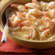 a bowl filled with shrimp and rice on top of a red cloth next to a spoon