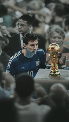 a man standing next to a golden trophy in front of a large group of people