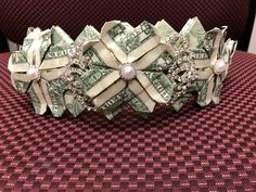 a bracelet made out of dollar bills with pearls and diamonds on it, sitting on top of a red table