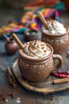 two mugs filled with whipped cream and cinnamon sticks