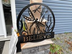 a metal clock sitting on top of a wooden post next to a building with dragonflies