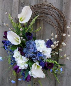 a wreath with flowers and greenery on top of a wooden wall next to a fence