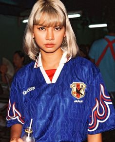 a woman with blonde hair wearing a blue shirt and holding a small object in her hand