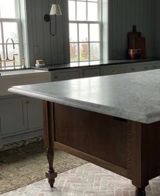 a large kitchen island with marble top in front of two windows and an open sink