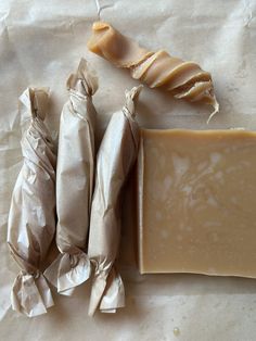 three pieces of soap sitting on top of a white paper covered table next to an unwrapped piece of wax