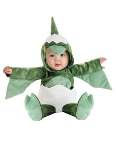 a baby in a green costume sitting on top of a white floor with his arms spread out