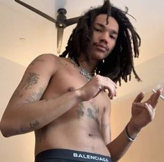 a shirtless man with dreadlocks is holding his cell phone and looking at the camera