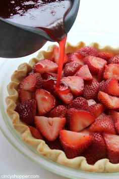 someone pouring syrup onto a pie crust filled with strawberries