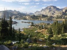 a lake surrounded by mountains and trees in the middle of a field with lots of rocks