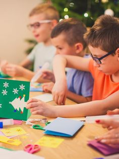 children are sitting at a table making christmas cards with construction paper and colored crayons