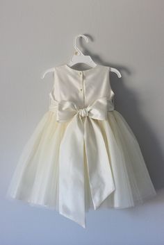 a white dress hanging on a wall with a hanger in front of it that has a bow at the waist