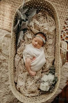 a newborn baby wrapped in a white wrap is laying on a wicker basket with flowers