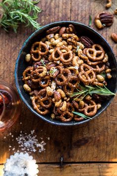 a bowl filled with nuts and rosemary on top of a wooden table next to a glass of wine