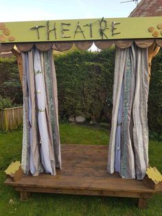 an outdoor stage with curtains and writing on the top that says theatre in front of it