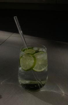 a glass filled with water and lime slices next to a straw on top of a table