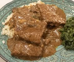 a blue plate topped with meat and gravy on top of rice next to broccoli