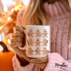 a woman holding a coffee mug with gingerbreads on it in front of a christmas tree