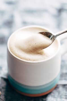 a spoon in a white cup filled with foamy liquid on top of a table