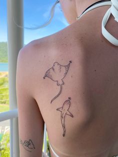 the back of a woman's shoulder with two dolphins tattoo on her left side