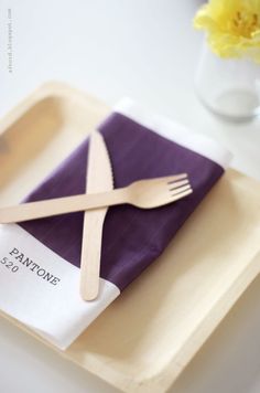 a fork and knife sitting on top of a purple napkin next to a yellow flower