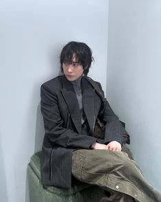 a man sitting on top of a green chair wearing a suit and tie with his hands in his pockets