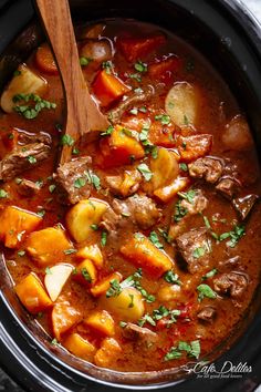 a crock pot filled with beef stew and potatoes, garnished with parsley