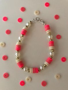 a pink and white beaded bracelet on a table with red buttoned circles around it