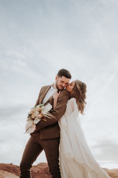 a bride and groom standing in the desert with their arms around each other as they kiss