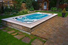 a hot tub sitting in the middle of a yard next to a brick walkway and fence