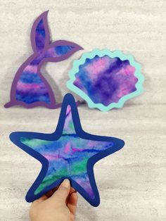 someone is holding up two starfish shaped magnets with purple, blue and green colors