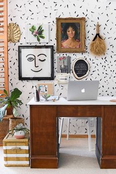 a desk with a laptop on it in front of a wall with pictures and paintings